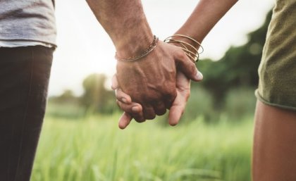 A couple holding hands while walking on the grass.